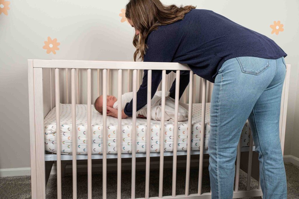 mother placing baby in crib while practicing safe sleep 